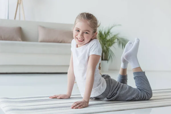 Glückliches kleines Kind macht Rückwärtsbeuge auf Yogamatte und schaut in die Kamera — Stockfoto