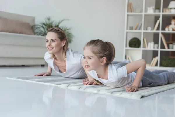 Мати і дочка роблять поштовхи разом на йога килимки вдома — стокове фото