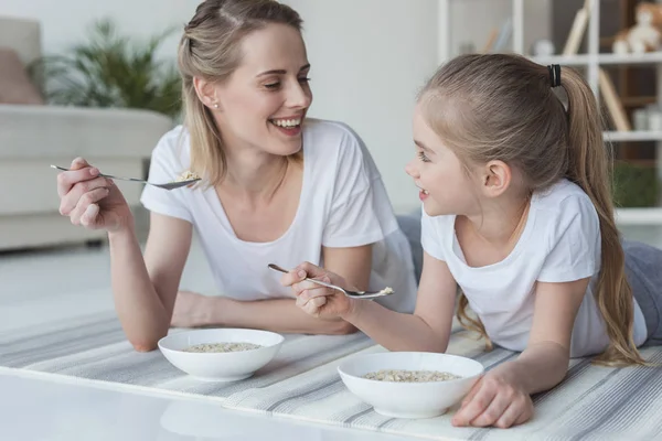 Happy mother and daughter eating cereal meal while lying on yoga mats — Stock Photo