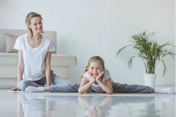 Mother sitting on floor with daughter while she doing twine — Stock Photo