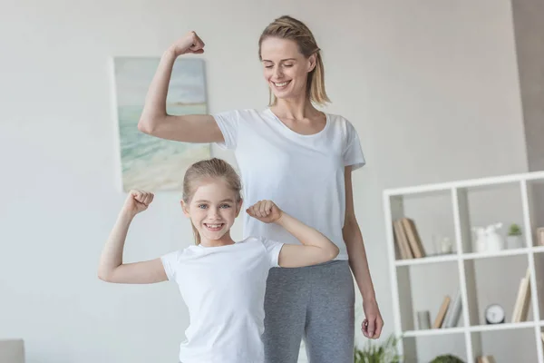 Happy fit mother and daughter showing biceps muscles — Stock Photo