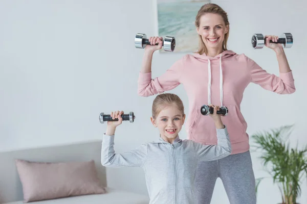 En forma madre e hija haciendo ejercicio con pesas en casa - foto de stock