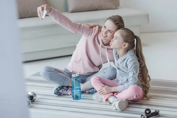 Mother and daughter taking selfie while sitting on yoga mat — Stock Photo