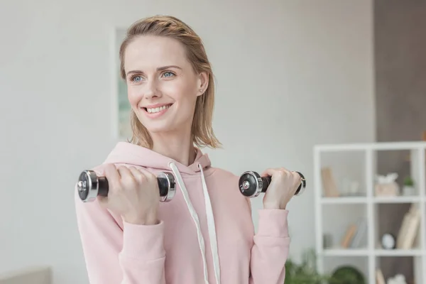 Attraktive lächelnde Frau, die zu Hause mit Hanteln trainiert — Stockfoto