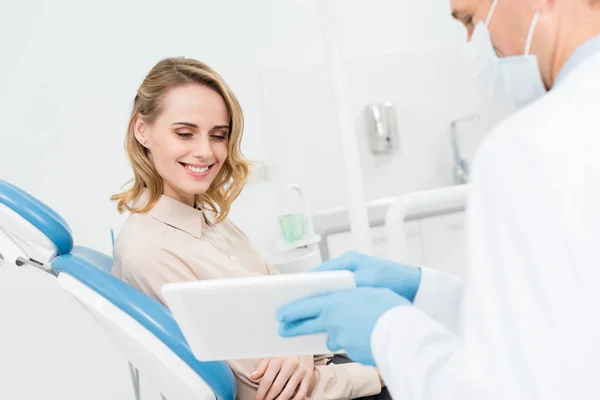 Doctor and smiling patient looking at tablet screen in modern dental clinic — Stock Photo