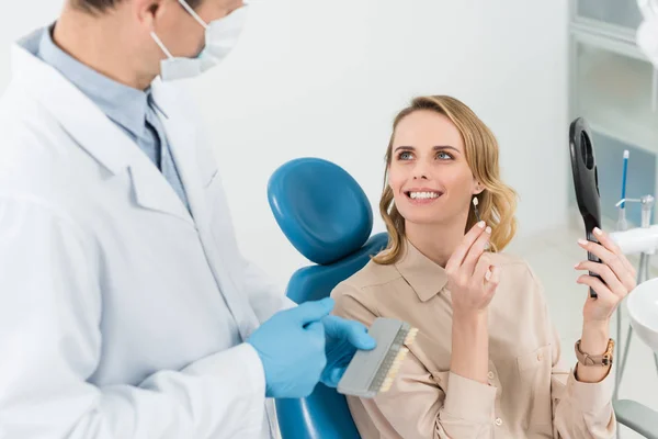 Woman consulting with doctor choosing tooth implant looking at mirror in modern dental clinic — Stock Photo