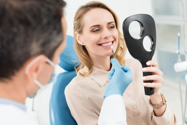 Paciente feminina escolhendo implante dentário olhando para o espelho na clínica odontológica moderna — Fotografia de Stock