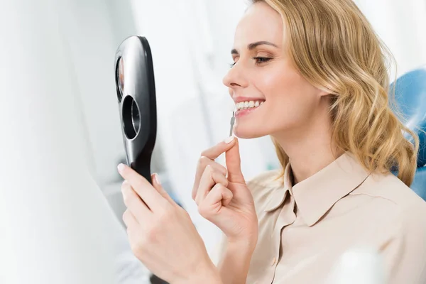 Жінка-пацієнтка вибирає імплантат зубів, дивлячись на дзеркало в сучасній стоматологічній клініці — стокове фото
