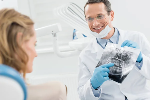 Odontólogo masculino que muestra radiografía de paciente femenino en clínica dental moderna - foto de stock