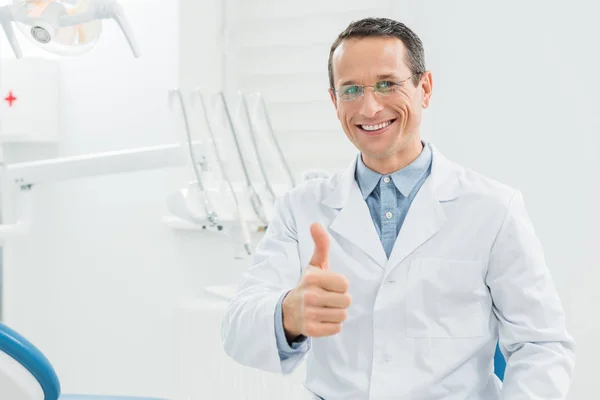 Dentista mostrando el pulgar hacia arriba en la clínica dental moderna - foto de stock