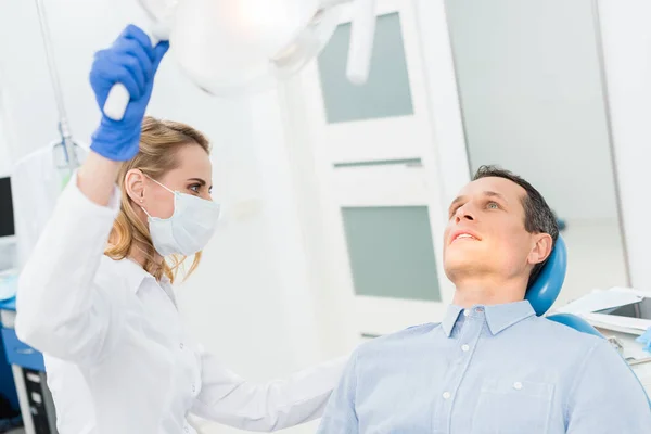 Mulher dentista ajustando lâmpada na clínica odontológica moderna — Stock Photo