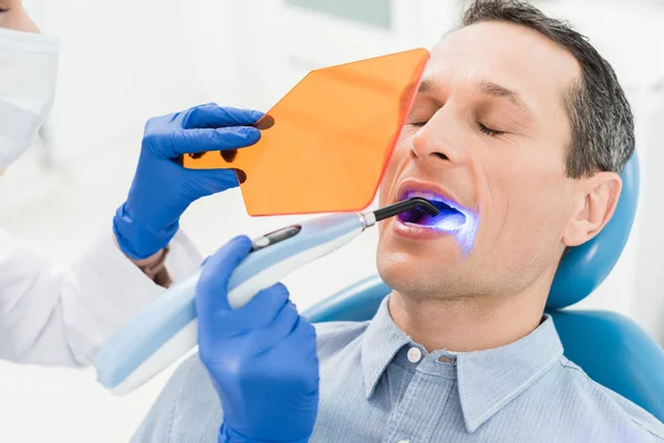 Patient masculin à la procédure dentaire en utilisant la lampe UV dans la clinique dentaire moderne — Photo de stock