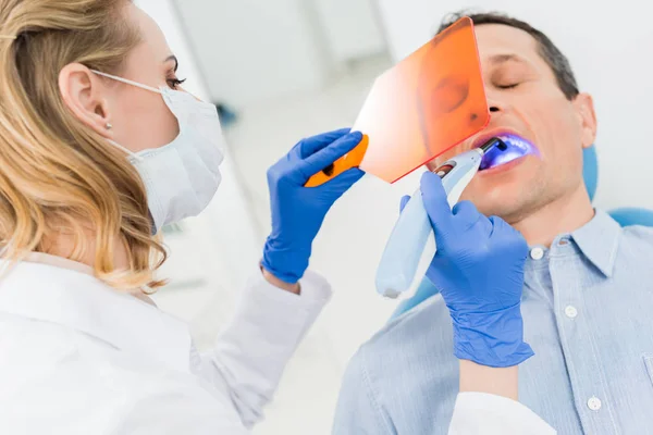 Dentist using uv lamp to treat patient teeth in modern dental clinic — Stock Photo