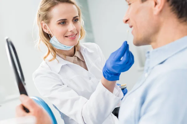 Paciente escolhendo implante dentário olhando para o espelho na clínica odontológica moderna — Fotografia de Stock