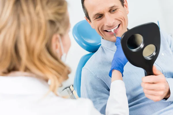 Uomo che sceglie l'impianto dentale guardando allo specchio nella moderna clinica dentale — Foto stock