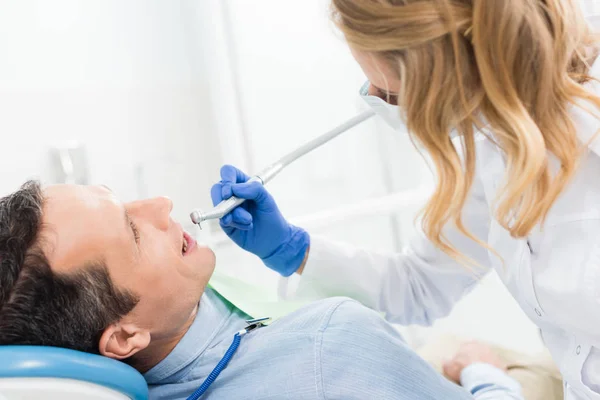 Пациент мужского пола на стоматологической процедуре с использованием зубной дрели в современной стоматологической клинике — стоковое фото