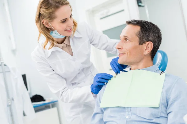 Doutor fixando guardanapo paciente masculino na clínica odontológica moderna — Fotografia de Stock