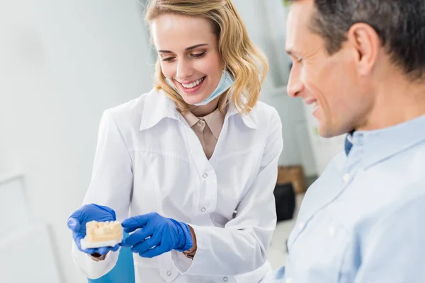 Médico e paciente olhando para o modelo de mandíbulas na clínica odontológica moderna — Fotografia de Stock