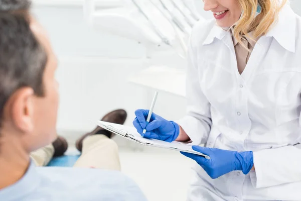 Diagnóstico de registro médico femenino en consulta con paciente en clínica dental moderna - foto de stock