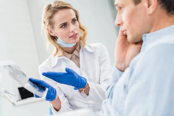 Homem consultoria com dentista olhando para raio-x na clínica moderna — Fotografia de Stock