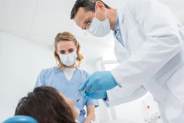 Odontólogo masculino y su asistente femenino revisando paciente en clínica dental moderna - foto de stock