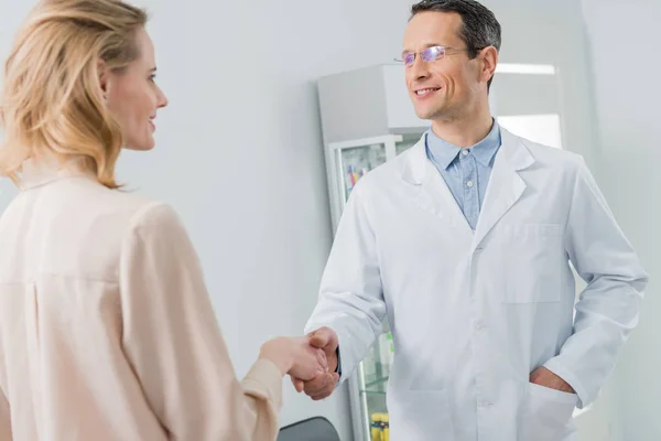Улыбающийся врач и пациентка пожимают руку в современной стоматологической клинике — стоковое фото
