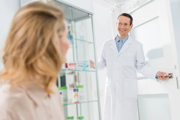 Médico sonriente dando la bienvenida a paciente femenina en clínica dental moderna - foto de stock