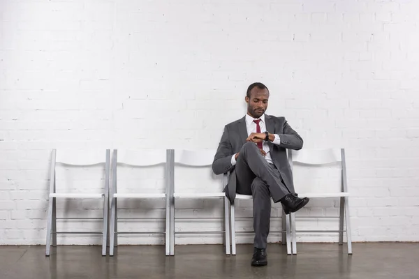 Hombre de negocios afroamericano comprobando el tiempo mientras espera entrevista de trabajo - foto de stock