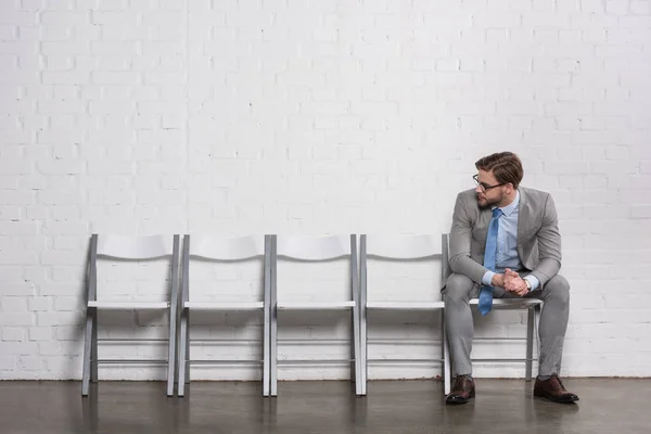 Hombre de negocios caucásico mirando sillas vacías mientras espera entrevista de trabajo - foto de stock