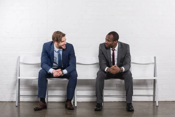 Lächelnde multikulturelle Geschäftsleute, die einander beim Warten auf ein Vorstellungsgespräch anschauen — Stockfoto