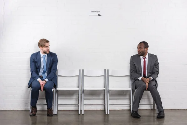 Hombres de negocios multiétnicos asustados mirándose mientras esperan una entrevista de trabajo - foto de stock