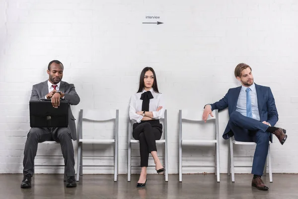 Jovens empresários multiétnicos sentados em cadeiras à espera de uma entrevista de emprego — Fotografia de Stock