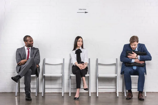 Jeunes gens d'affaires multiethniques assis sur des chaises en attendant un entretien d'embauche — Photo de stock