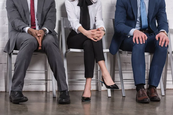 Visión parcial de los empresarios multiétnicos sentados en sillas mientras esperan una entrevista de trabajo - foto de stock