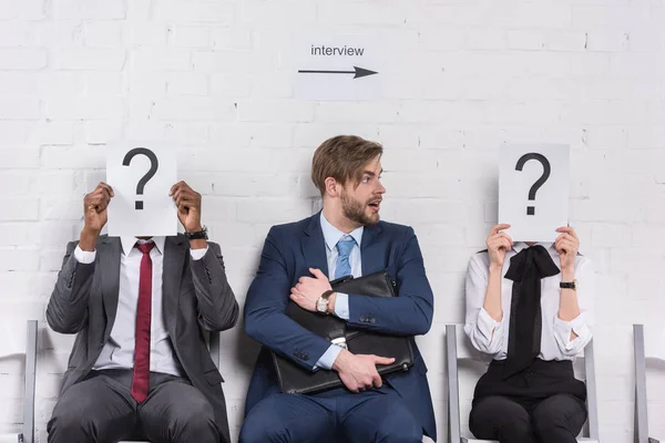 Caucasian businessman and multiethnic business people holding cards with question marks while waiting for job interview — Stock Photo