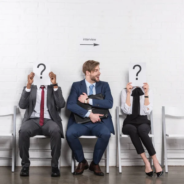 Caucasian businessman and multiethnic business people holding cards with question marks while waiting for job interview — Stock Photo