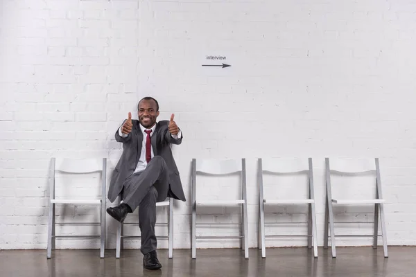 Hombre de negocios afroamericano mostrando pulgares hacia arriba mientras espera entrevista de trabajo - foto de stock