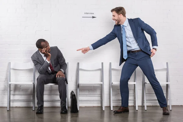 Aufgeregter kaukasischer Geschäftsmann zeigt auf einen afrikanisch-amerikanischen Kollegen, der auf ein Vorstellungsgespräch wartet — Stockfoto