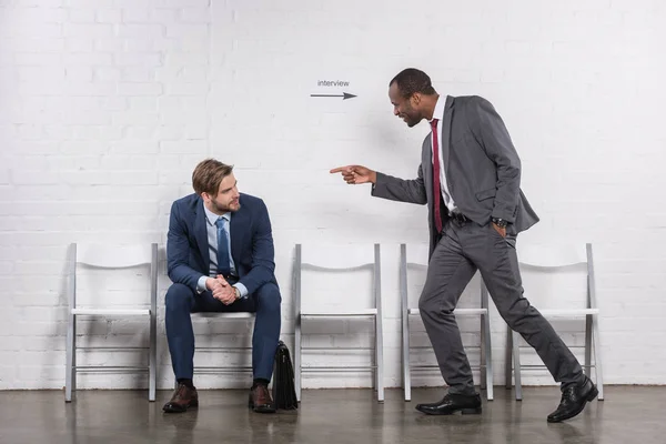 Hombre de negocios afroamericano apuntando a colega caucásico que espera entrevista de trabajo - foto de stock