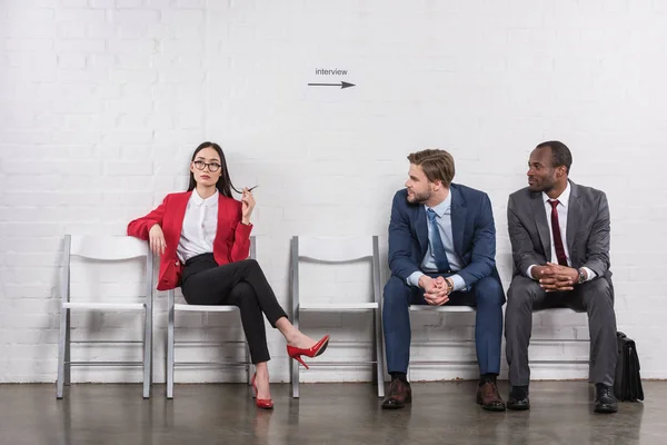 Multicultural homens de negócios olhando para asiático empresária enquanto espera para emprego entrevista — Fotografia de Stock