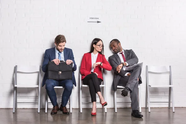 Gente de negocios multiétnicos sentados en sillas mientras espera entrevista de trabajo - foto de stock