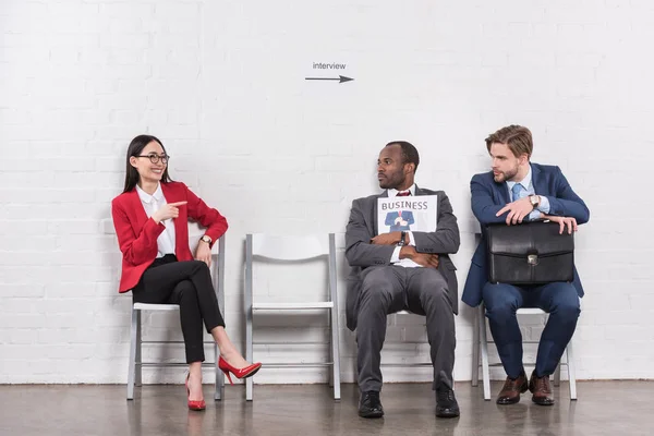 Smiling asian businesswoman pointing at multiethnic businessmen while waiting for job interview — Stock Photo