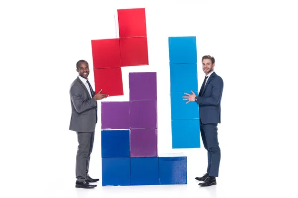 Vista lateral de sonrientes hombres de negocios multiétnicos con bloques de colores aislados en blanco, concepto de trabajo en equipo - foto de stock