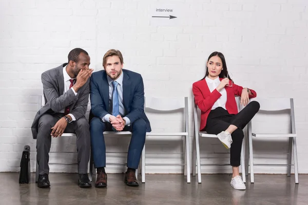 Asiático mujer de negocios mirando multicultural hombres de negocios chismorreo mientras espera para trabajo entrevista - foto de stock