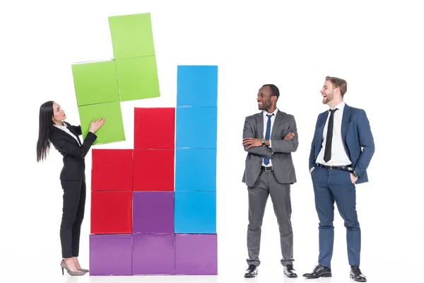 Multicultural businessmen looking at asian businesswoman collecting colorful blocks isolated on white, teamwork concept — Stock Photo