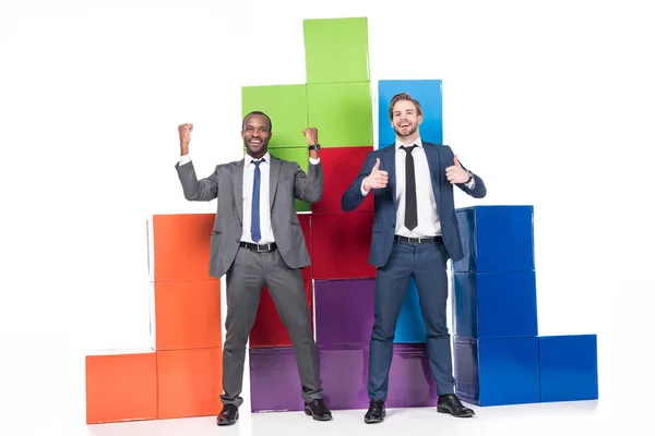 Felici uomini d'affari multietnici in piedi vicino blocchi colorati isolati su bianco, lavoro di squadra e concetto di successo — Foto stock