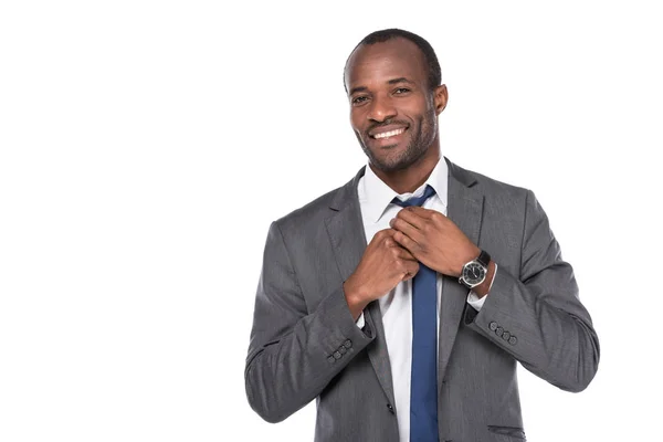 Retrato de alegre hombre de negocios afroamericano atando pajarita aislada en blanco - foto de stock