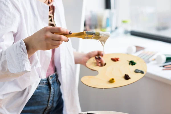 Jeune fille artistique tenant la palette avec de la peinture en studio léger — Photo de stock