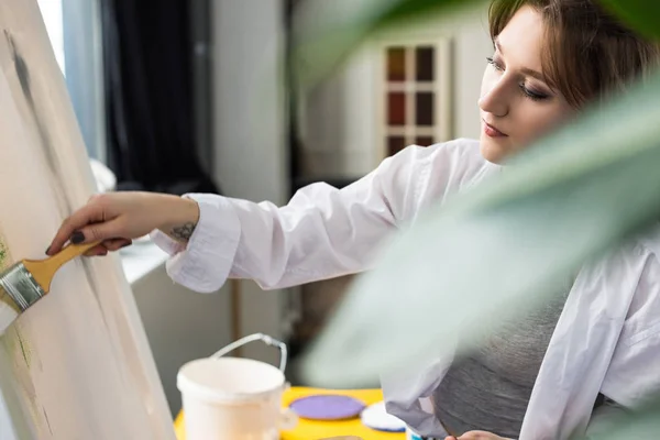 Young artistic girl painting at easel in light studio — Stock Photo