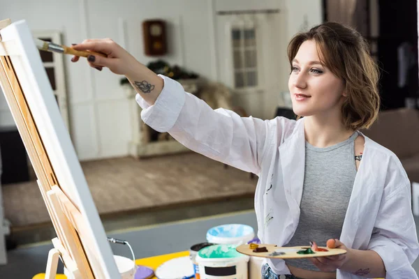 Young inspired girl working by easel in light studio — Stock Photo